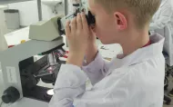 Chłopiec w fartuchu  przy mikroskopie